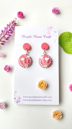 the pink and yellow earrings are sitting on top of a card next to some flowers