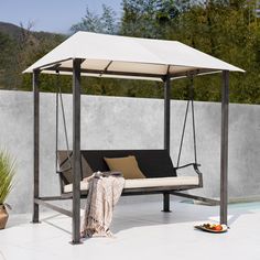 an outdoor swing chair with a canopy and pillows on the ground next to a pool