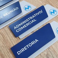 three blue and white name tags sitting on top of a wooden table next to each other