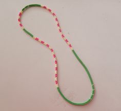 a green beaded necklace with pink beads on a white surface, next to a red and yellow ribbon