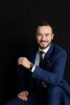 a man in a suit and tie sitting on a stool with his arms crossed, smiling at the camera