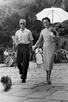 an old black and white photo of a man and woman holding hands while walking their dog