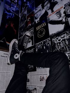 a man in black pants and sneakers leaning against a wall with posters on the walls