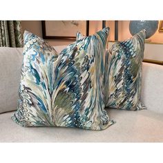 two blue and green pillows sitting on top of a white couch next to a lamp