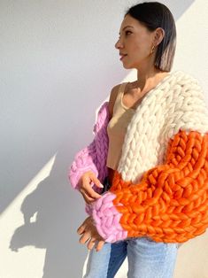 a woman wearing an orange, white and pink knitted sweater standing in front of a wall