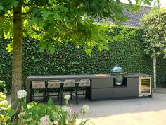 an outdoor kitchen with grill and chairs in front of a wall covered with greenery