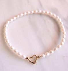 Size 5-6mm rice-shaped freshwater pearl bracelet with 14K gold heart centerpiece in a stretchy cord. Wear it alone or layer it on.  Strung by hand in our Los Angeles studio. Classic White Heart Bracelet For Gifts, Elegant Heart-shaped Pearl Bracelet With Charm, Elegant Heart-shaped Pearl Charm Bracelet, Elegant White Pearl Bracelet For Valentine's Day, Adjustable Heart Bracelet With Pearl Charm, Elegant Heart Beads Stretch Bracelet Gift, Elegant Heart Beads Stretch Bracelet For Gift, Elegant Round Beads Stretch Bracelet For Valentine's Day, Elegant White Pearl Bracelet With Heart Charm