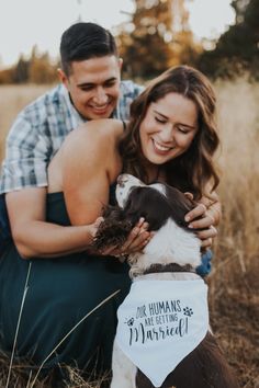 a man and woman sitting next to a brown and white dog wearing a bib