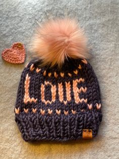 "All you need is Love Beanie, is set in soft pink words and subtle heart border, then framed in beautiful navy blue background. A warm winter toque that will get the looks as you set the tone letting people know \"Love\" is the answer to what we really need.  This hat is ready to ship and sized for circumference 21-22.5\" for average ladies and is approximately 9\" tall.  This soft squishy, fair isle knit toque is made with chunky acrylic yarn, in navy & pink. The top has a luxury faux fur Pom ties on and trimmed with a leather logo tag that says Hugs & Stitches on the outside and \"handmade with love\" on the inside! Pattern is adapted from the word beanie designs from Lady Jay Crochet. *hats should be hand washed paying careful attention to not submerge Pom, ans lay flat to dry. All shop Pink Warm Hat As A Gift, Pink Warm Hat For Gift, Warm Pink Hat For Gift, Jay Crochet, Pink Winter Hat, Pink Words, Knit Toque, Love Is The Answer, Heart Border