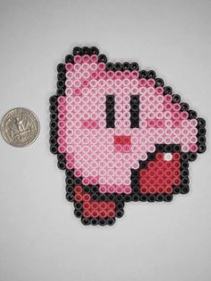 a penny sitting next to a pink pixel art piece on a white surface with the face of an animated character made out of legos