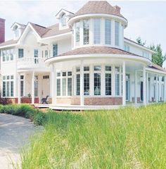 a large white house sitting on top of a lush green field next to tall grass