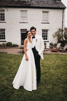 a bride and groom standing in front of a large white house with grass on the lawn