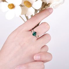 a woman's hand with a ring on her finger and flowers in the background