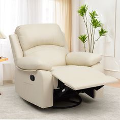 a white recliner chair with a footstool in front of a window and a potted plant