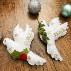 two white birds decorated with green leaves and red berries on top of a wooden table