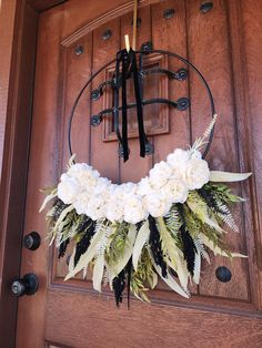 a wreath with white flowers and black ribbon hangs on the front door of a house