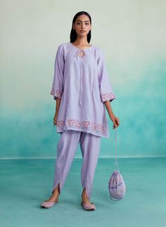 Introducing our ethereal lavender kurta set - a captivating two-piece ensemble crafted in fine chanderi fabric. The kurta features intricate hand embroidery, delicate mirror work, and elegant hangings for added grace. Paired with ankle-length tulip pants, this set exudes charm and style. Complete your enchanting look with matching juttis and elevate your wardrobe with this ethereal masterpiece today! Chikankari Chanderi Pant Set For Navratri, Navratri Chikankari Chanderi Pant Set, Chanderi Pant Set With Chikankari Embroidery And Straight Kurta, Summer Cotton Silk Kurta With Mirror Work, Festive Cotton Pant Set With Mirror Work, Purple Cotton Silk Straight Kurta, Purple Gota Work Straight Kurta Sets, Purple Straight Kurta Sets With Gota Work, Traditional Lavender Sets With Mirror Work