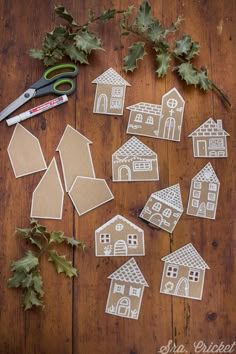 some cut out houses are sitting on a wooden table next to scissors and greenery