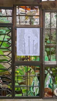 a stained glass window with green leaves and flowers in the center, behind it is a piece of artwork