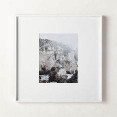 a white framed photograph hanging on a wall next to a wooden frame with an image of snow covered mountains in the background