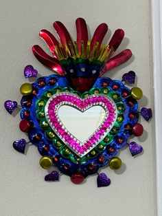 a colorful heart shaped mirror hanging on the side of a white wall next to hearts