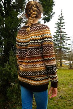 a woman standing in front of a tree wearing a sweater with braids on it