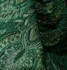 green paisley fabric with gold sequins on the bottom and side, close up