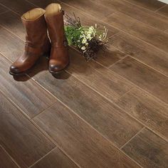 a pair of brown boots sitting on top of a wooden floor next to a potted plant