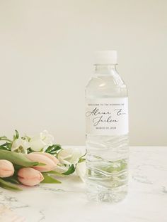 a bottle of water sitting on top of a table next to some pink and white flowers