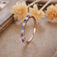 a gold ring with blue and white stones on the side, sitting next to flowers