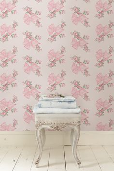 a white bench sitting in front of a wall with pink flowers and leaves on it