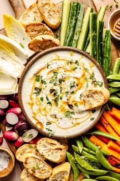 an assortment of vegetables, bread and dip in a bowl on a wooden platter