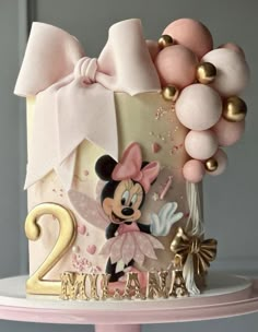 a birthday cake decorated with balloons and a minnie mouse figurine for two year old