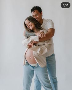 a man and woman hugging each other while standing in front of a white wall