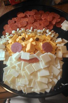 a pizza face made out of cheese and pepperoni on a black plate with other toppings