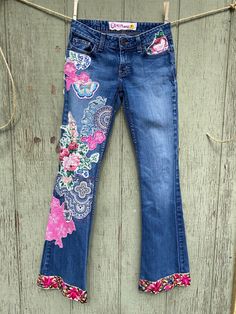 a pair of blue jeans hanging on a clothes line with flowers and butterflies painted on them