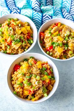 three bowls filled with rice and vegetables on top of a blue table cloth next to a fork