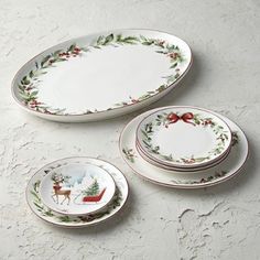 three plates with holly wreath designs on them, one has a bow and the other has a deer