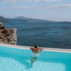 a man swimming in a pool next to the ocean with mountains in the back ground