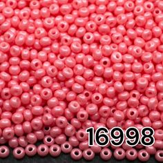 pink seed beads with holes in the middle on a black background and one red bead is