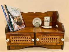 a wooden bench with plates and cups on it, next to a magazine rack filled with books