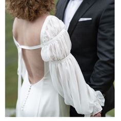 the back of a woman's white dress with ruffles on it and a man in a tuxedo