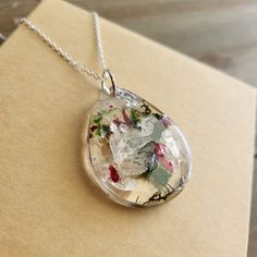 Beautiful White Baby's Breath, Red Rose Flower, And Green Moss Necklace With Real Colorful Flowers In Resin. Delicate Babys Breath Buds Paired With Garnet Red Flowers. Colorful Hues Mingle Together To Create This Naturally Stunning Terrarium Jewelry Piece. Each Pendant Is Uniquely Off-Rounded With Warbling Edges For An Artistic, And Magnifying Affect. This Necklace Pendant Is Two Sided, One Is Smooth And Magnifying, And The Other Is Textured With Real Flowers, Naturally Preserved For Eternal Bea Flower Necklace With Lobster Clasp As Gift, Flower Pendant Necklace With Lobster Clasp As Gift, Lily Pad Flower, Moss Necklace, Turquoise Cross Necklace, Gray Beaded Necklace, Flowers In Resin, Ivory Necklace, Beaded Boho Necklace