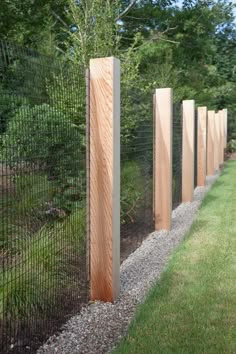 a row of wooden posts on the side of a fenced in area with grass and trees