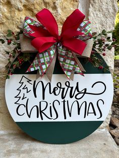 a merry christmas sign hanging on the side of a stone wall with a red bow