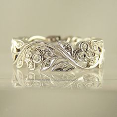 an intricately designed wedding band is shown in this image, with its reflection on the surface