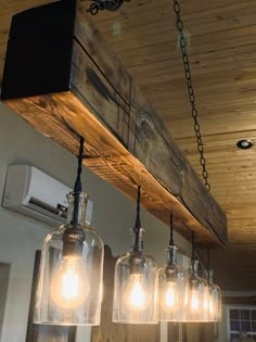 the lights are hanging from the wooden beam in the kitchen area, which is decorated with glass jars and wood planks