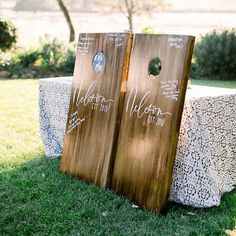 two wooden boards with writing on them sitting in the grass next to a white table cloth