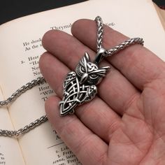 a hand holding a book with a silver necklace on it's side and an open book in the background