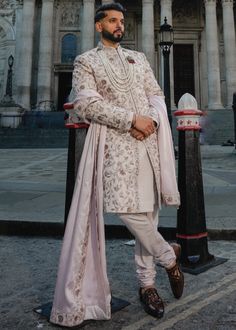 a man standing in front of a building wearing a white and beige sherve